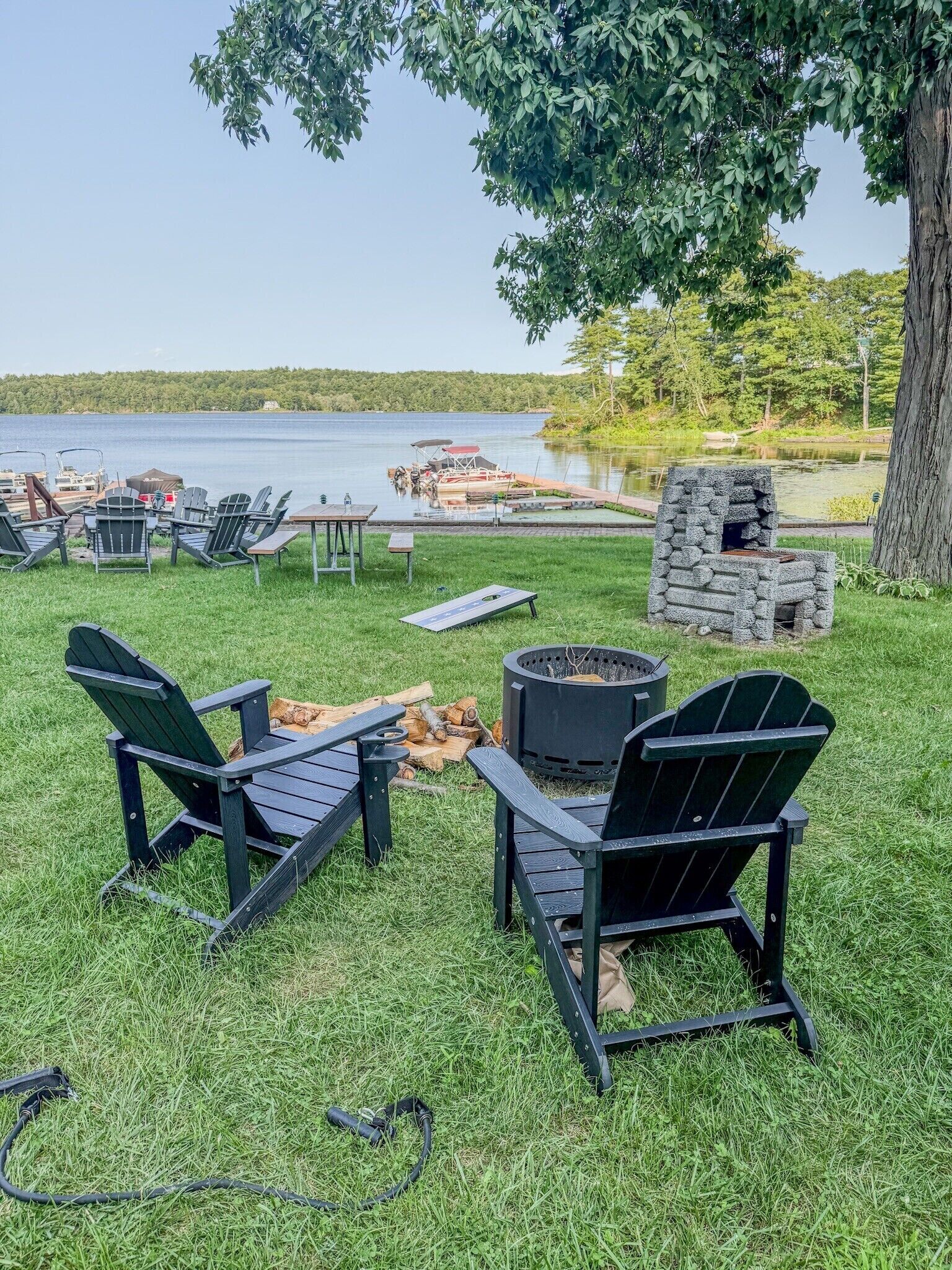 An outdoor seating area with Adirondack chairs, a fire pit, and a stone structure, overlooking a body of water.