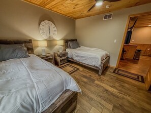 A bedroom with two beds, a wooden ceiling, a wall clock, and a small kitchenette. - Lakeside Loft on Black Lake (Hammond)