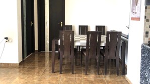 Un espace repas comprenant une table et des chaises, une porte noire et un revêtement de sol carrelé.