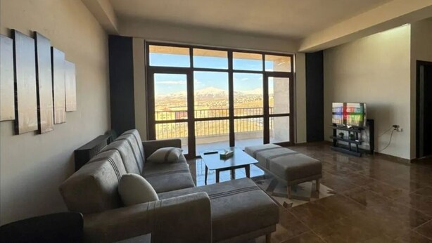 Un salon spacieux avec une grande fenêtre, un canapé, une table basse et un meuble pour la télévision.