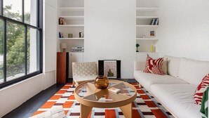 A modern living room with a sofa, a coffee table, and a patterned rug. There are bookshelves and a chair in the room.
