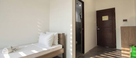 A hotel room with a bed, a wooden headboard, a white pillow, a towel, and a door leading to a bathroom.