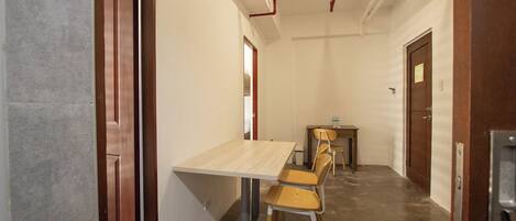 A narrow hallway with a wooden door on the left, a white wall, and a small table with chairs in the center.