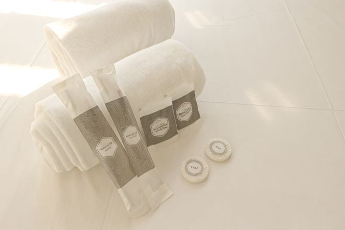A stack of white towels and a bottle of hand soap on a white tiled floor.