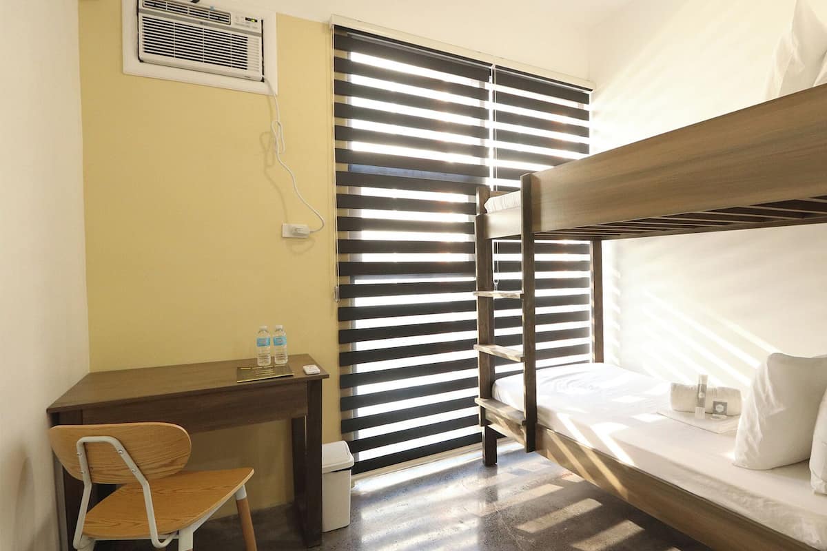 Habitación con literas, escritorio, silla y ventana con persianas.