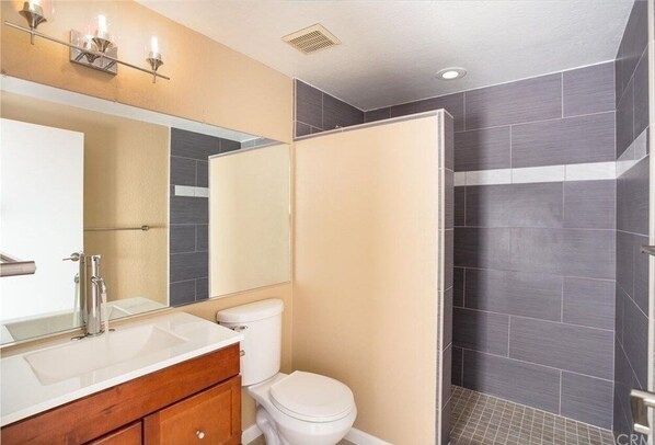 A bathroom with a white sink, a mirror, a toilet, and a shower area with dark tiles.