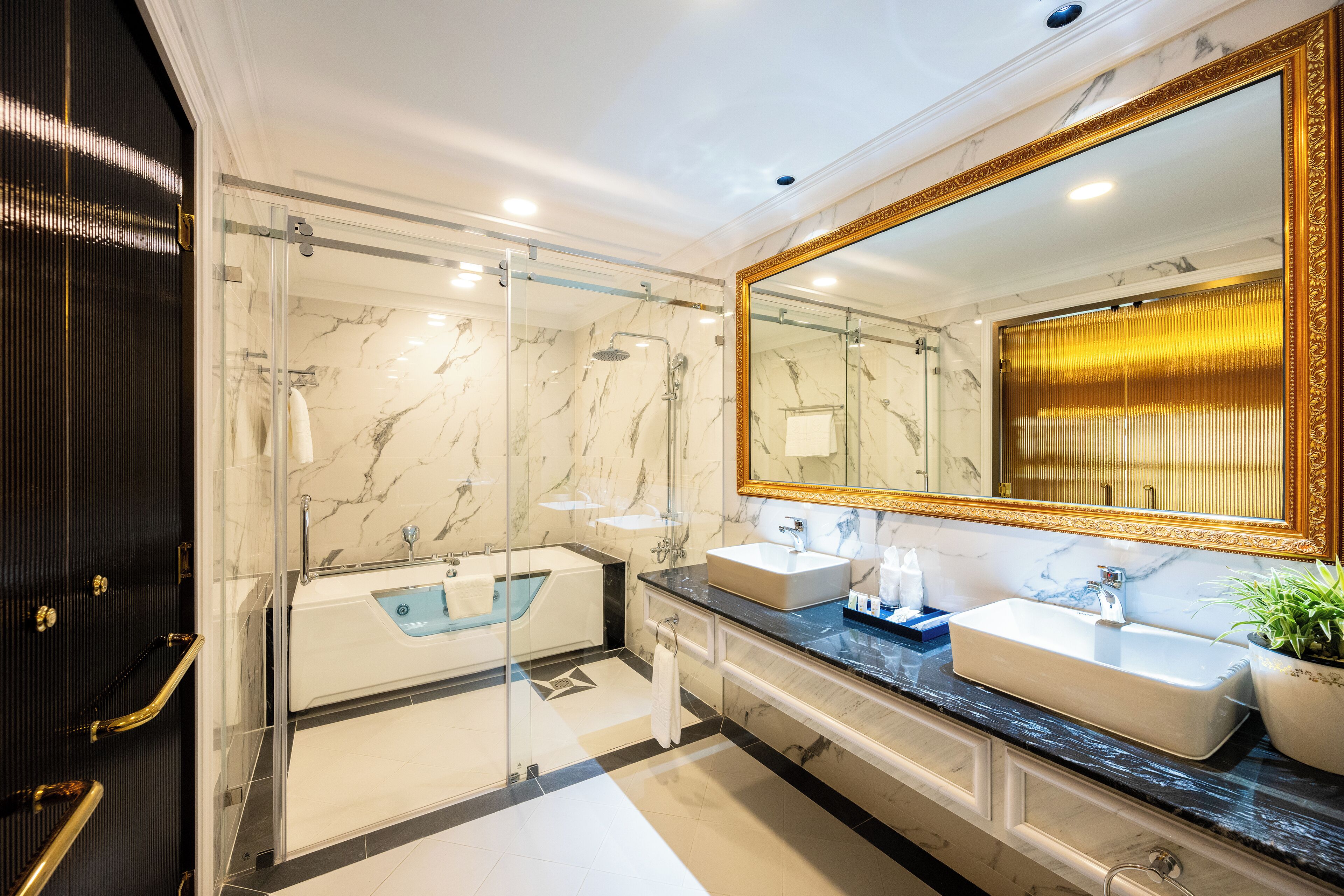 A modern bathroom with a glass-enclosed shower, two sinks, and a large mirror with a gold frame.