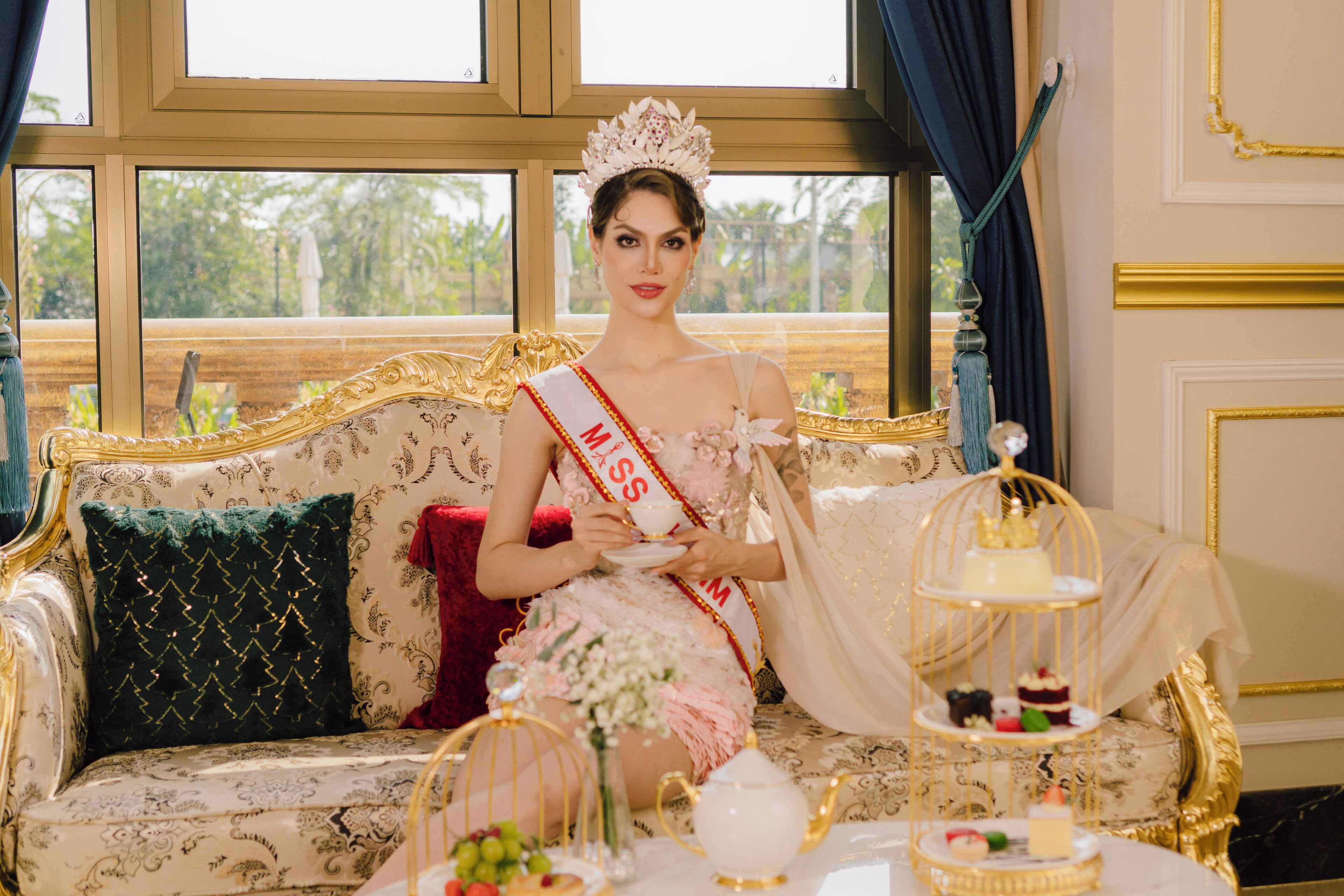 Une personne assise sur un canapé richement décoré, avec une fenêtre en arrière-plan.