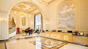 A grand lobby with a marble reception desk, a grand piano, and a staircase leading to upper floors. - LaChateau (Ho Chi Minh City)