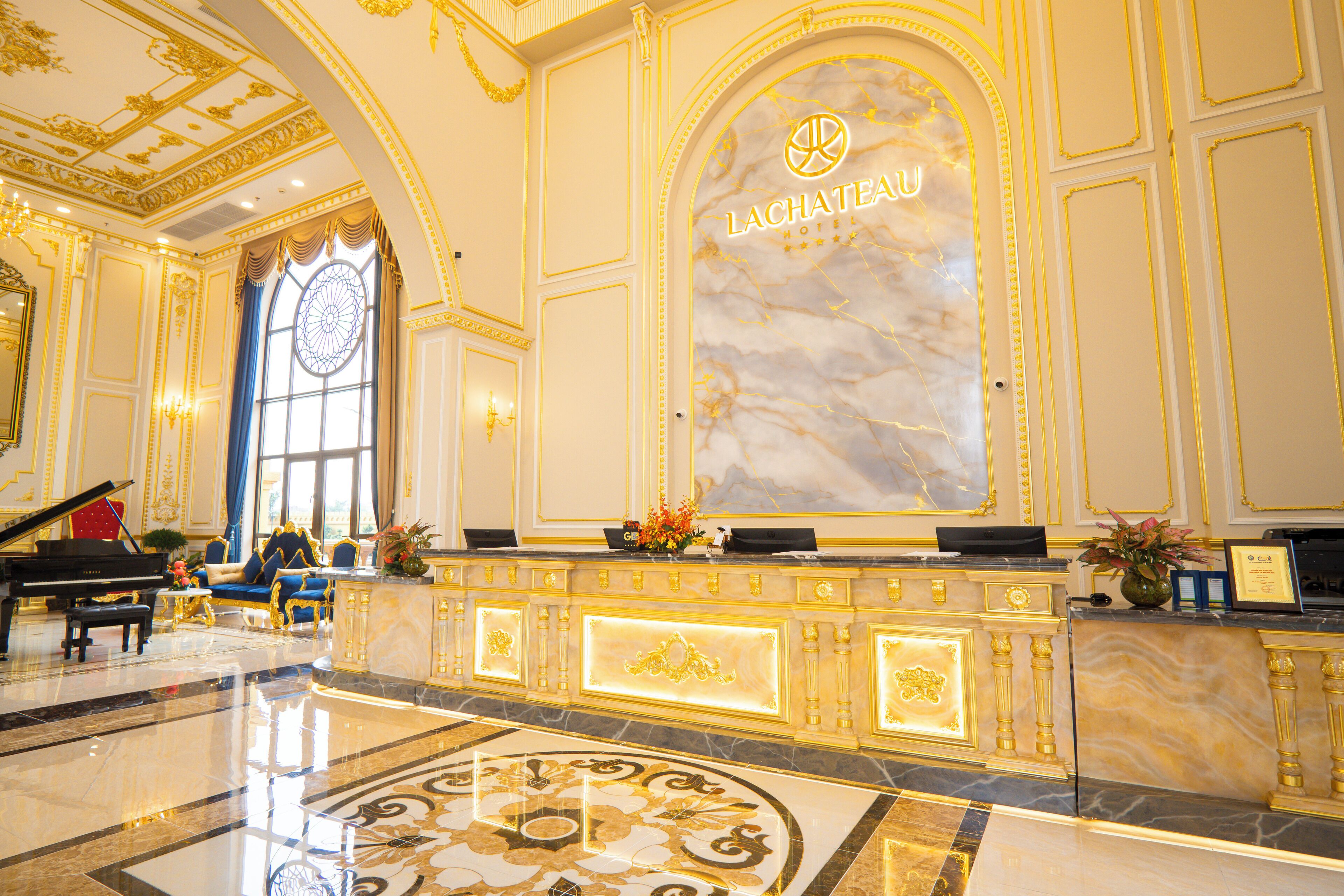 A grand lobby with a reception desk, a grand piano, and a large arched window.