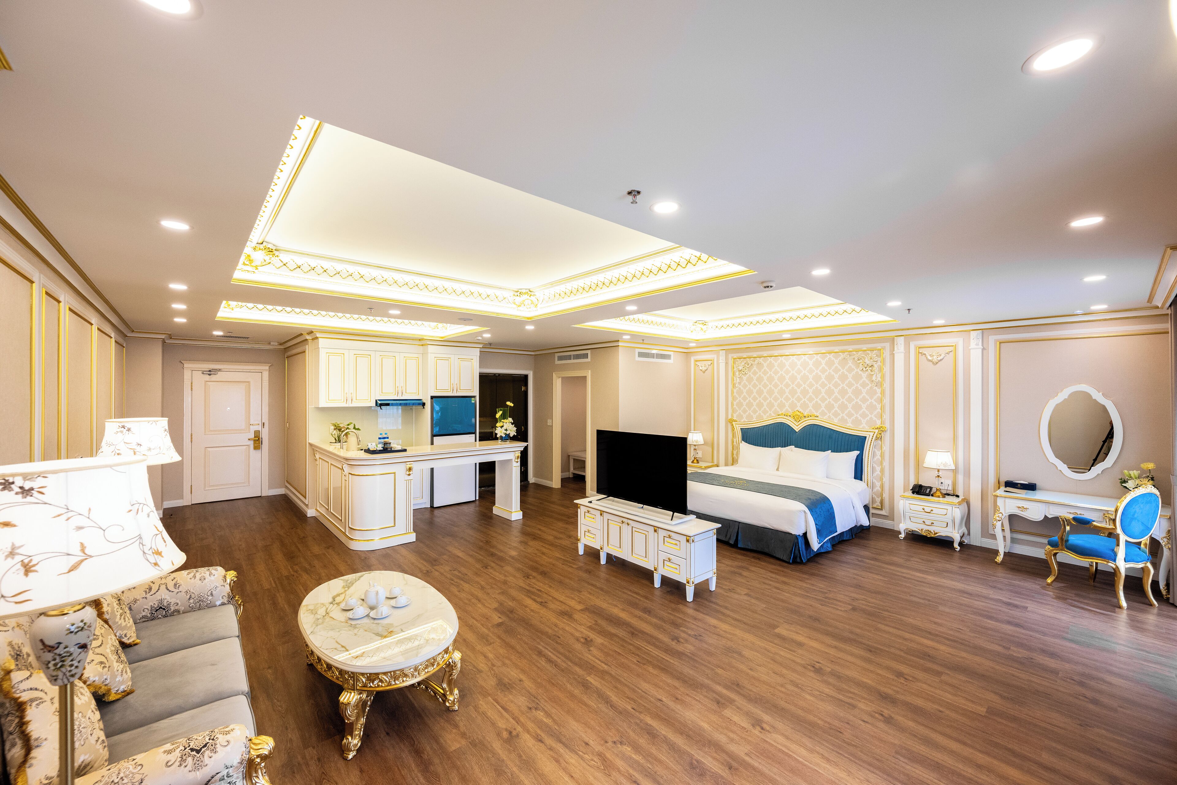A spacious hotel room with a large bed, a desk, a television, and a seating area with a table and chairs.