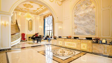 Un amplio vestíbulo con una imponente recepción de mármol, un piano de cola y una escalera que conduce a los pisos superiores.