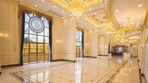 A spacious lobby with ornate gold detailing, large windows with blue curtains, and a chandelier. - LaChateau (Ho Chi Minh City)
