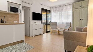 A modern kitchen with white cabinets, a microwave, and a flat-screen TV. There is a dining area with a beige sofa and a wooden table. - Montemar Puerto - Beachfront, Terrace, Swimming Pool. Sea Views (Torremolinos)