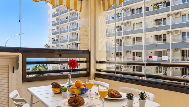 A balcony with a table set for breakfast, including croissants, fruit, and juice, overlooking a residential building. - Montemar Puerto - Beachfront, Terrace, Swimming Pool. Sea Views (Torremolinos)
