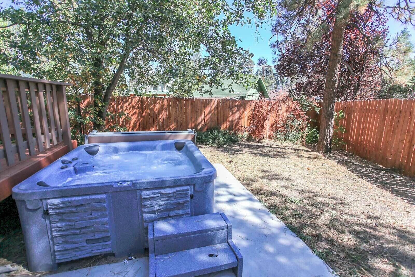 Jacuzzi con revestimiento de piedra y escalones, rodeado por una terraza de madera y una valla de madera.