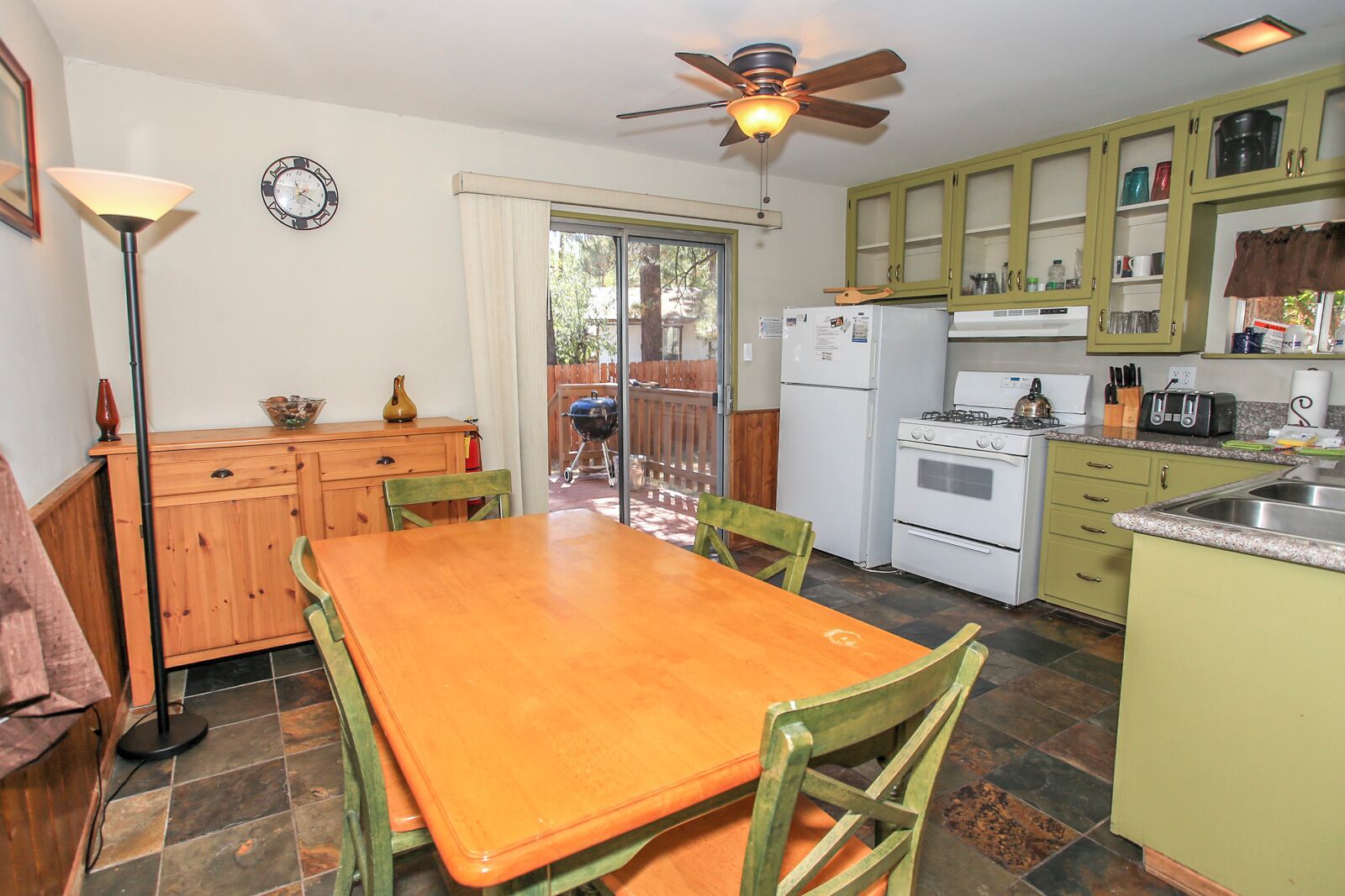 A kitchen with a wooden table and chairs, a ceiling fan, and green cabinets.