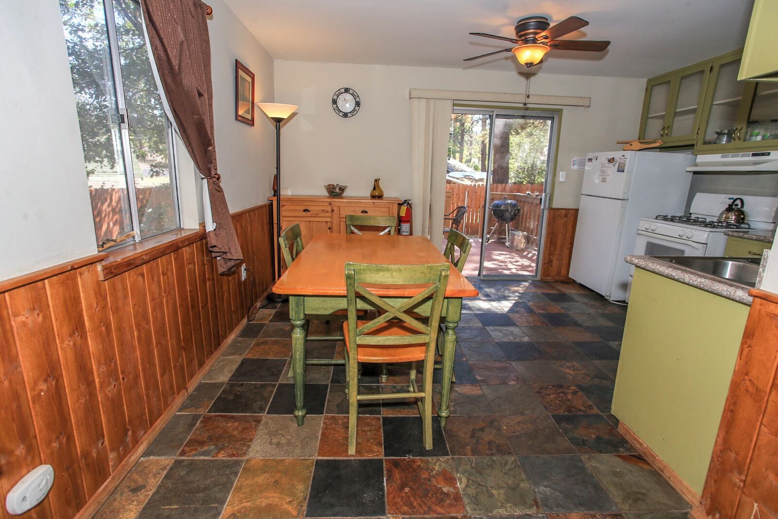 A compact kitchen with a dining table and chairs, a ceiling fan, and a view through a glass door to an outdoor area.