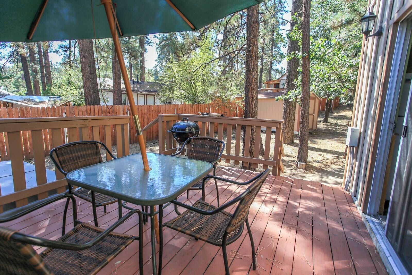 A wooden deck with a glass table and chairs, surrounded by a wooden fence and trees.