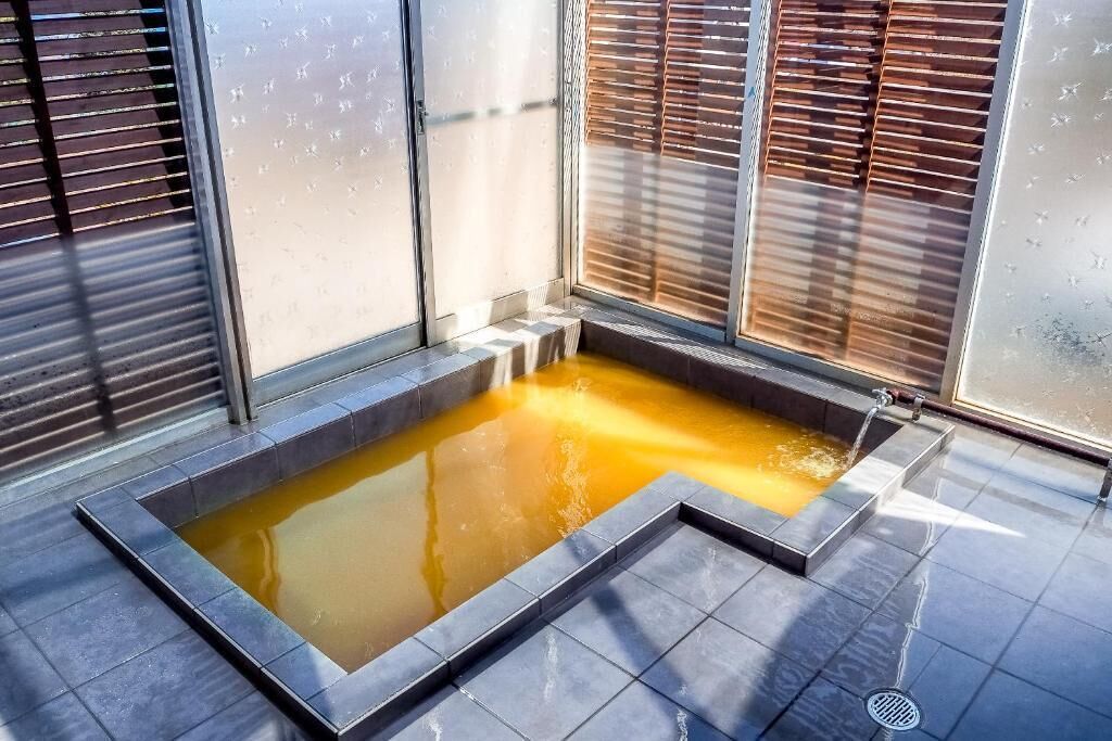 A spa area with a rectangular hot tub, tiled flooring, and wooden blinds.