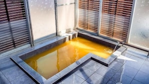 Ein Wellnessbereich mit einem rechteckigen Whirlpool, Fliesenböden und Holzjalousien.