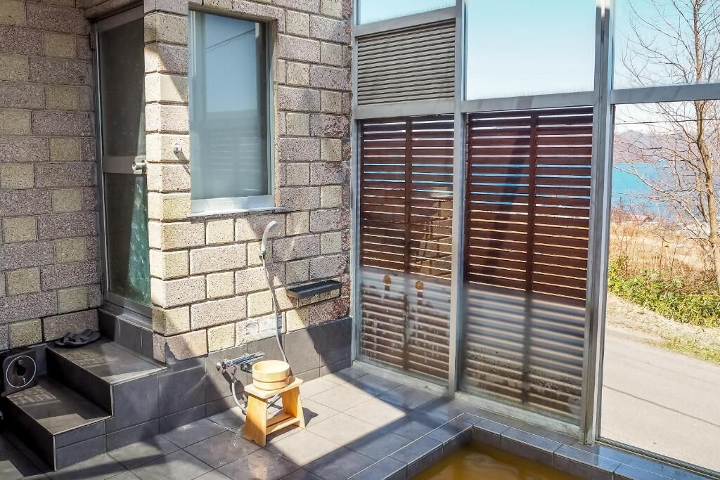 A modern bathroom with a stone wall, a window, a wooden stool, and a small water feature.