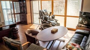 Ein geräumiges Wohnzimmer mit großem Fenster, Massagesessel, rundem Tisch und Ledersofa.