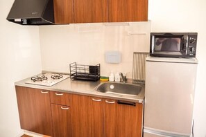 A compact kitchen with wooden cabinets, a stainless steel sink, a microwave, and a black range hood. - TOYA ONSEN VILLA (Usu-gun, Sobetsu-cho, Sobetsu ONSEN)