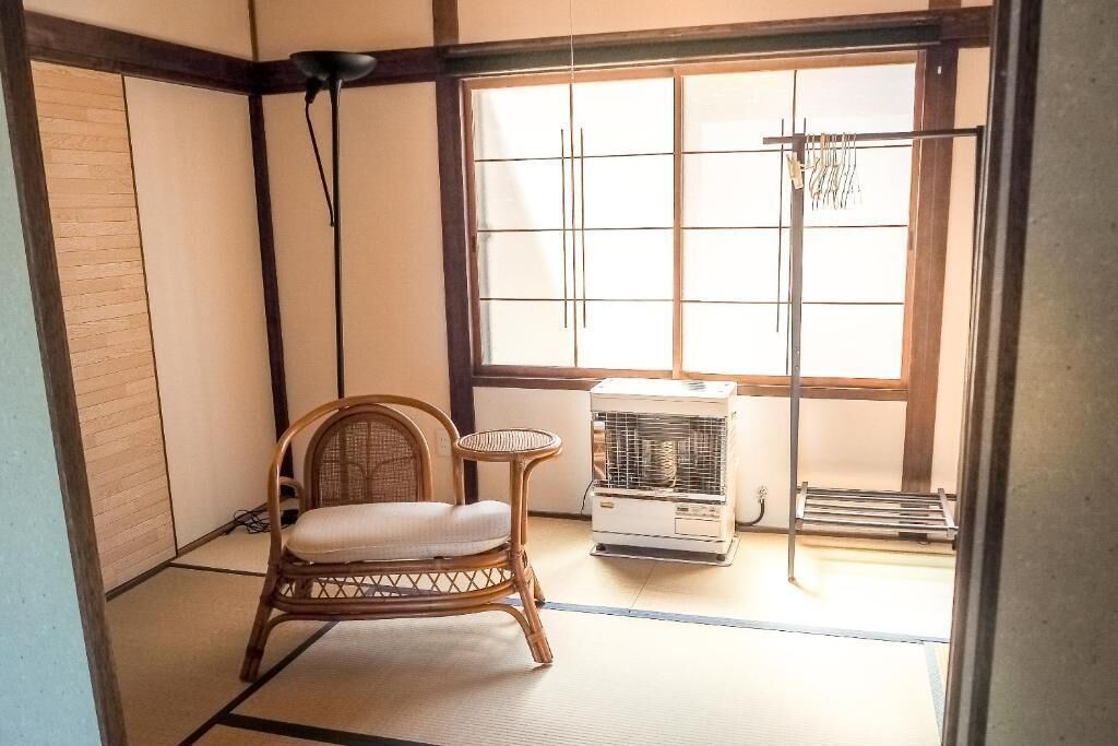 Una habitación japonesa tradicional con suelo de tatami, una silla de bambú, una pequeña mesa y un calentador.