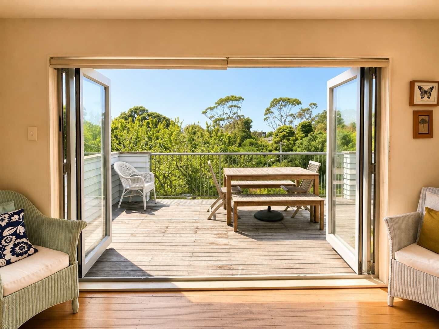 Une pièce dotée d’une porte-fenêtre coulissante donnant sur un balcon extérieur, où se trouvent une table et des chaises en bois.