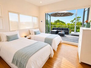 Habitación de hotel con dos camas, un balcón con sofá y mesa, y vista a zonas verdes.