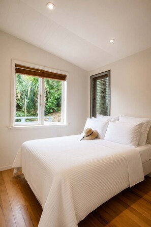 Une chambre à coucher avec un lit, du linge de lit blanc, une fenêtre donnant sur un paysage verdoyant et un plafond doté d’un éclairage encastré.