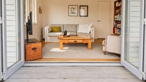 A living room with a sofa, coffee table, and a bookshelf. - Beachlovers Onetangi - Walk to Onetangi Beach (Waiheke Island)
