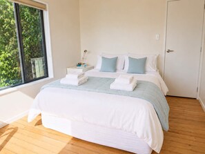 Un dormitorio con cama, almohadas, mesita de noche y ventana.