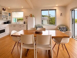 Una cocina moderna con armarios blancos, una mesa de comedor de madera y sillas. Hay una ventana que ofrece vistas a zonas verdes.