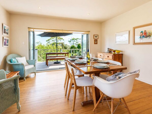 Un comedor con una mesa de madera dispuesta para cuatro personas, una silla de mimbre y vistas al exterior.