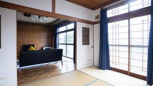 A traditional Japanese room with tatami flooring, a black sofa, and a sliding door with blue curtains. - Gray house toya (Toyako)