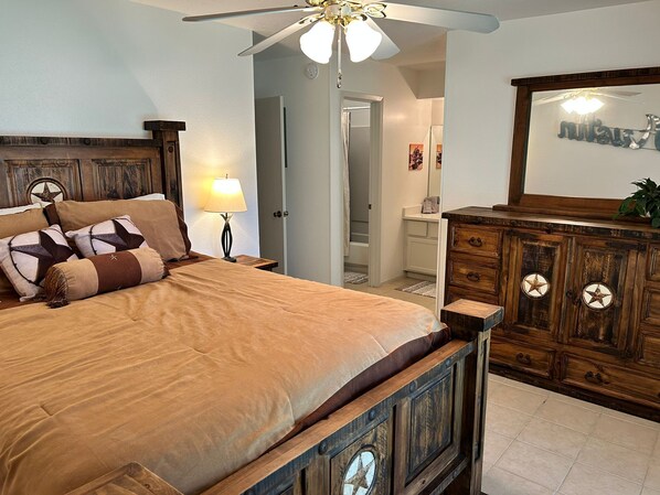 A bedroom with a wooden bed, a nightstand with a lamp, a dresser with a mirror, and a ceiling fan. - Upscale: 20 min DT, fenced yard, garage, all utils (Austin)