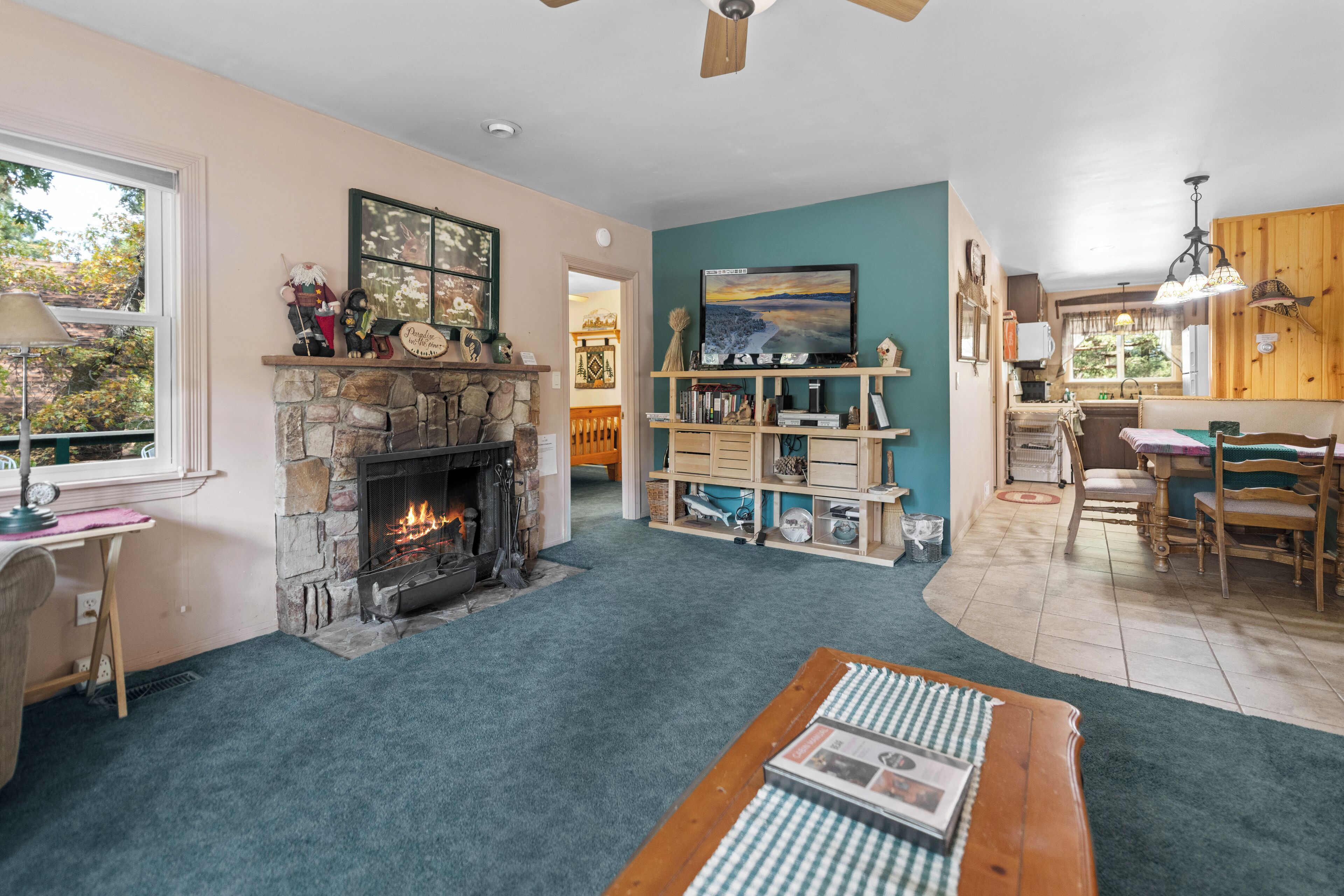 A cozy living room with a stone fireplace, a wooden coffee table, and a bookshelf.