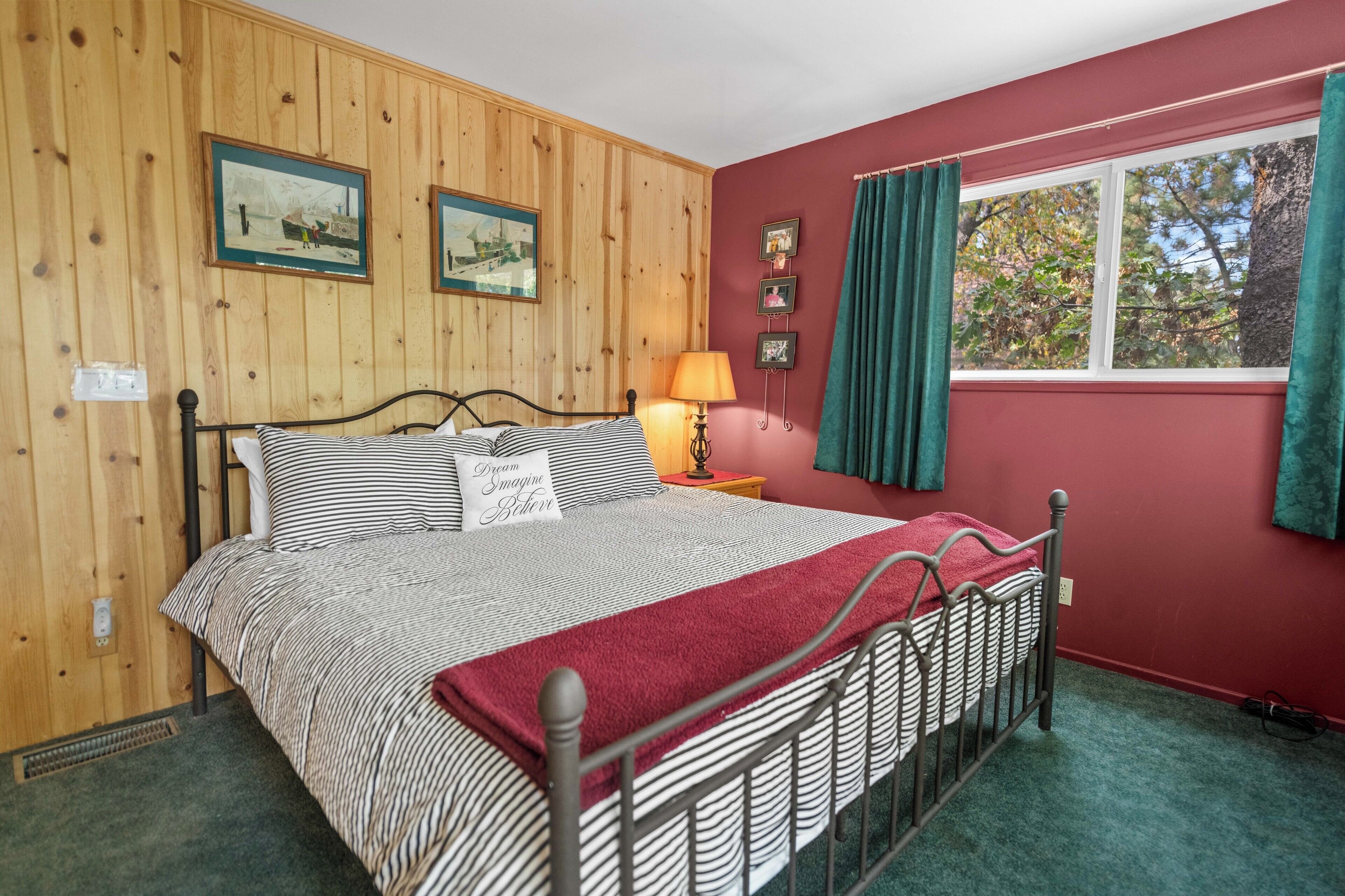 Un dormitorio con cama, paredes de paneles de madera, ventana con cortinas e imágenes enmarcadas en la pared.