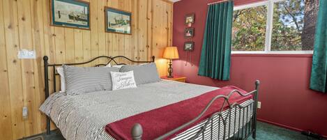 Un dormitorio con cama, paredes de paneles de madera, ventana con cortinas e imágenes enmarcadas en la pared.