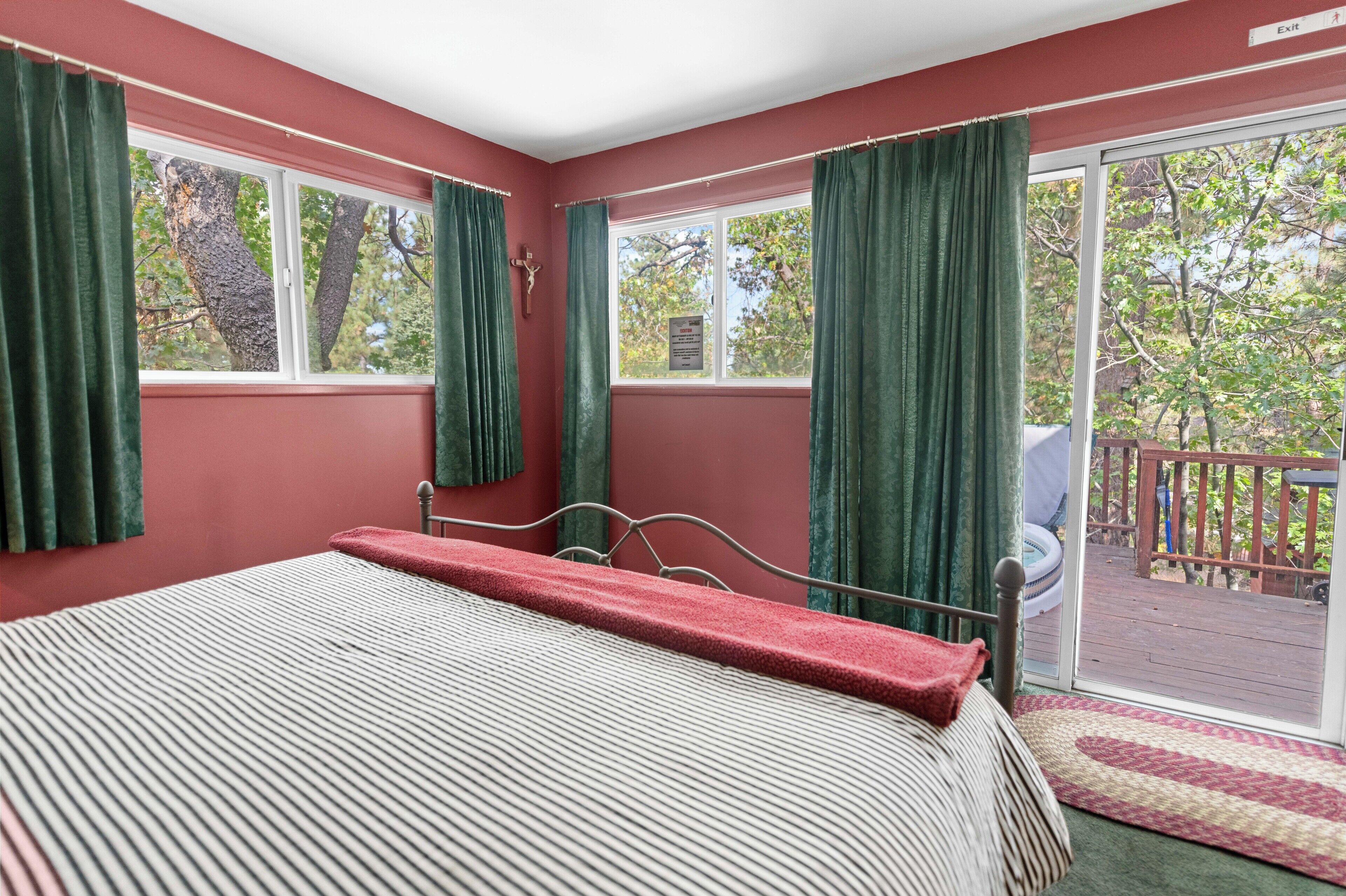 A bedroom with a bed, green curtains, a window, and a view of a deck.
