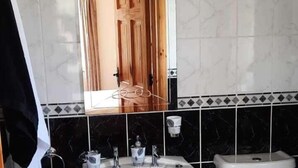 Une salle de bain avec une porte en bois, des carreaux de marbre noir et un lavabo blanc.