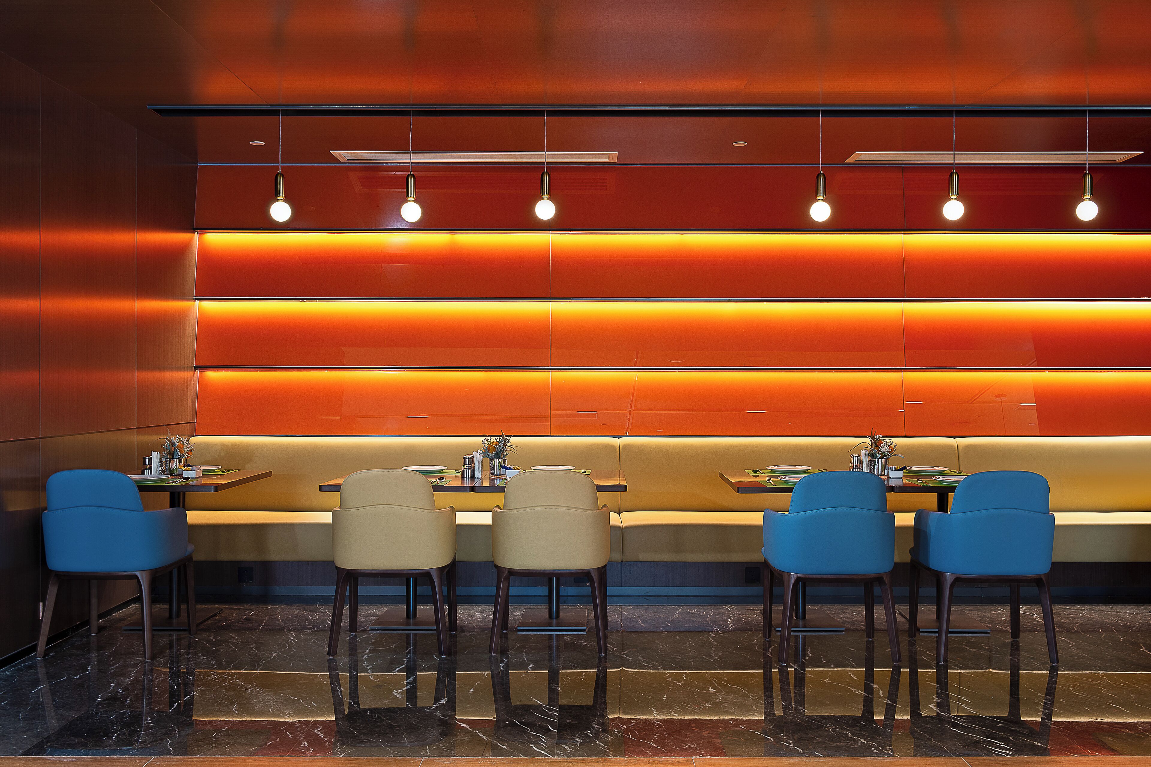A modern restaurant with a long counter, blue chairs, and a neon-lit wall.