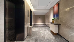 Un pasillo moderno con piso de mármol, un cesto de basura y un mostrador de recepción con una planta en maceta.