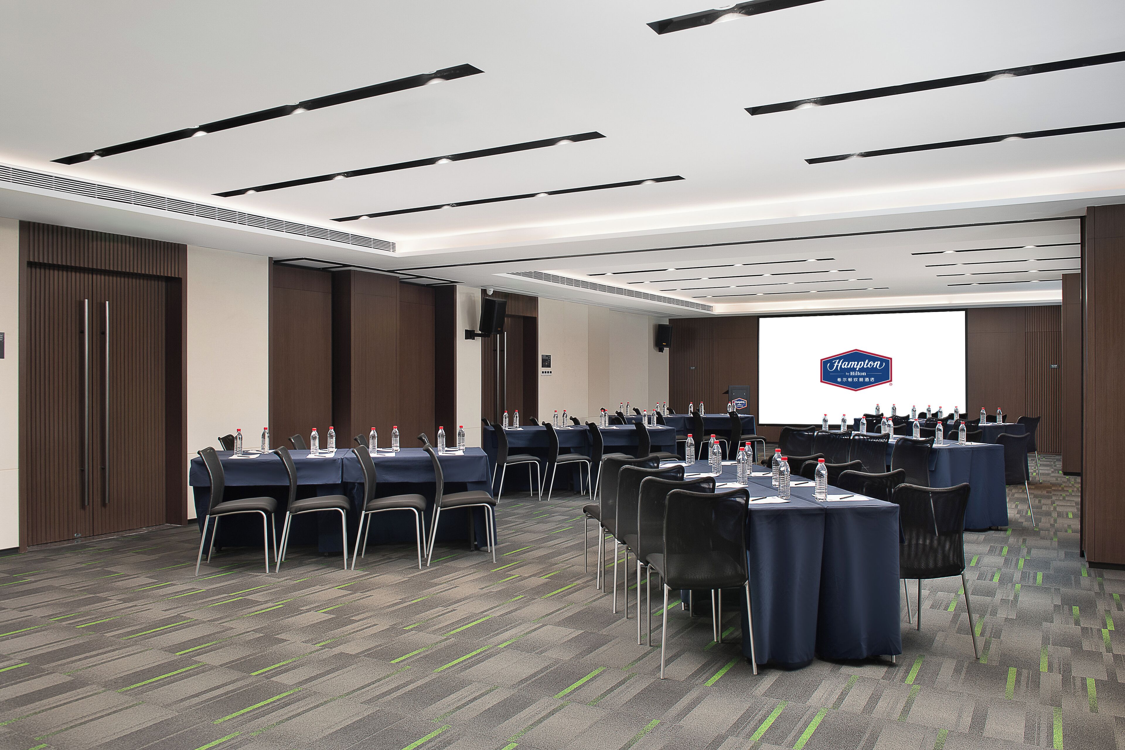 A conference room with multiple tables, chairs, and a projection screen displaying a logo.