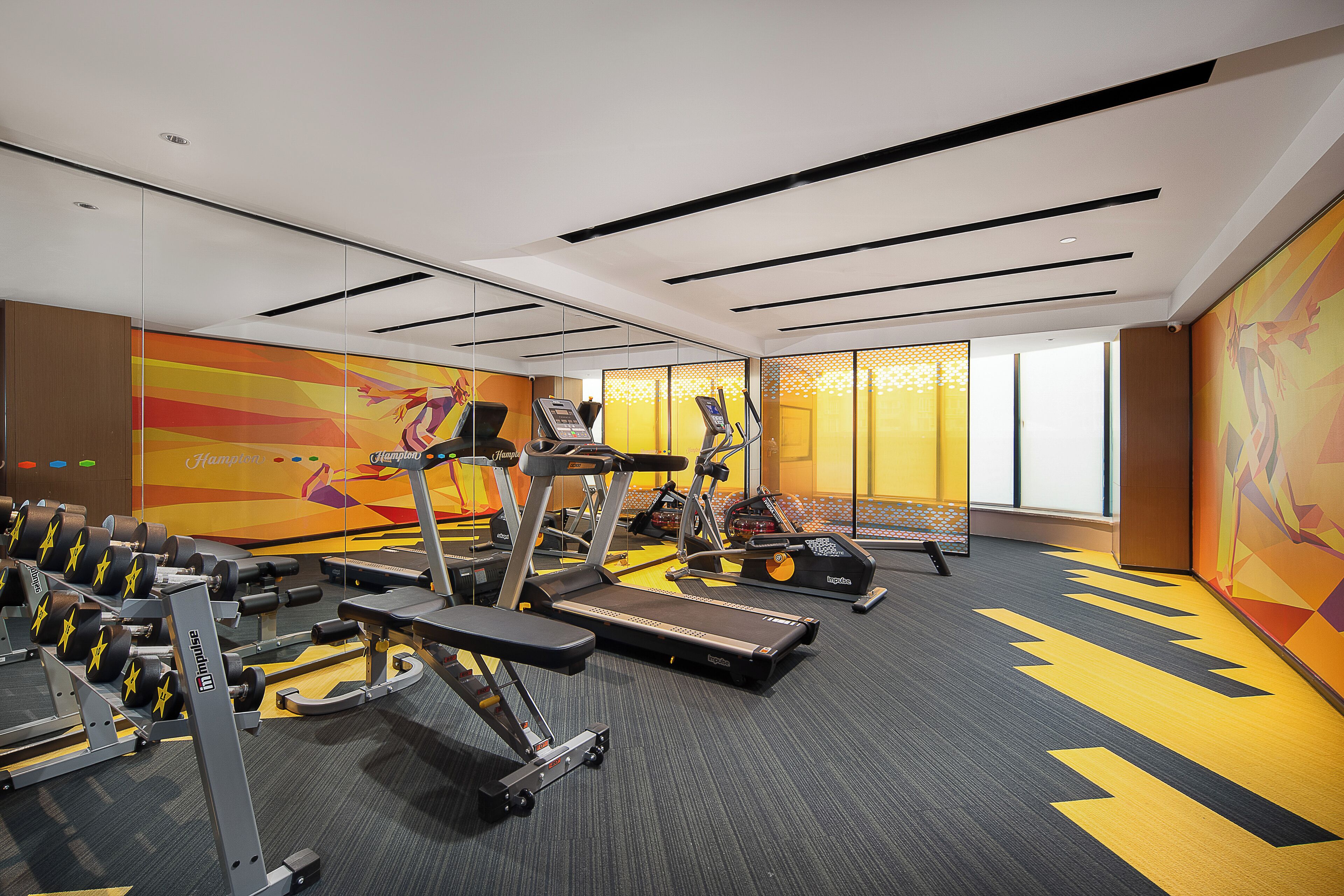 Une salle de sport équipée de tapis de course, d’appareils de musculation et ornée d’une fresque murale aux couleurs vives.