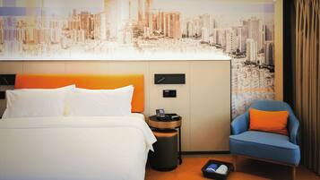 A hotel room with a bed, a chair, a nightstand, and a cityscape mural on the wall.