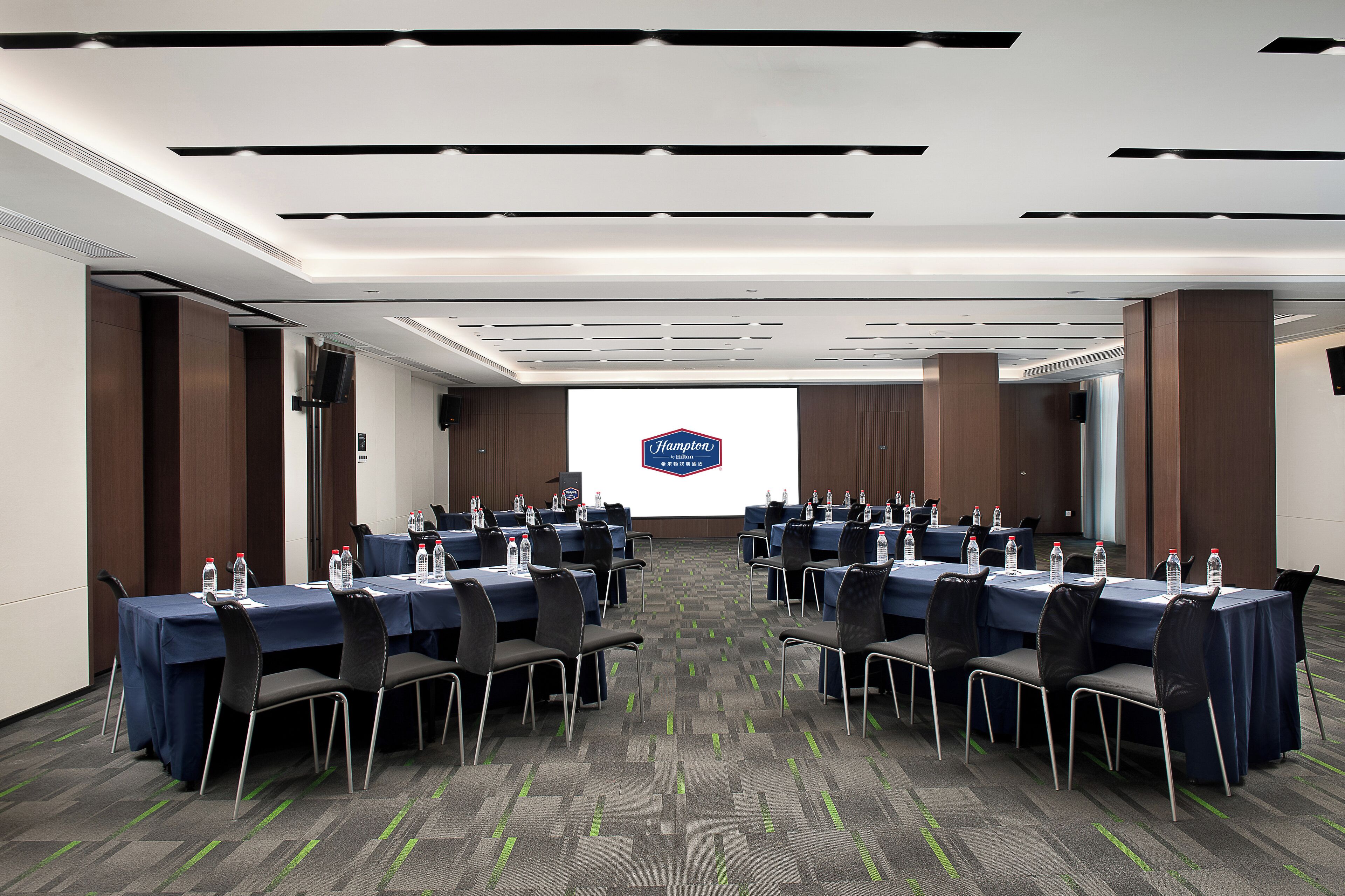 A conference room with multiple tables, chairs, and a large screen displaying a logo.