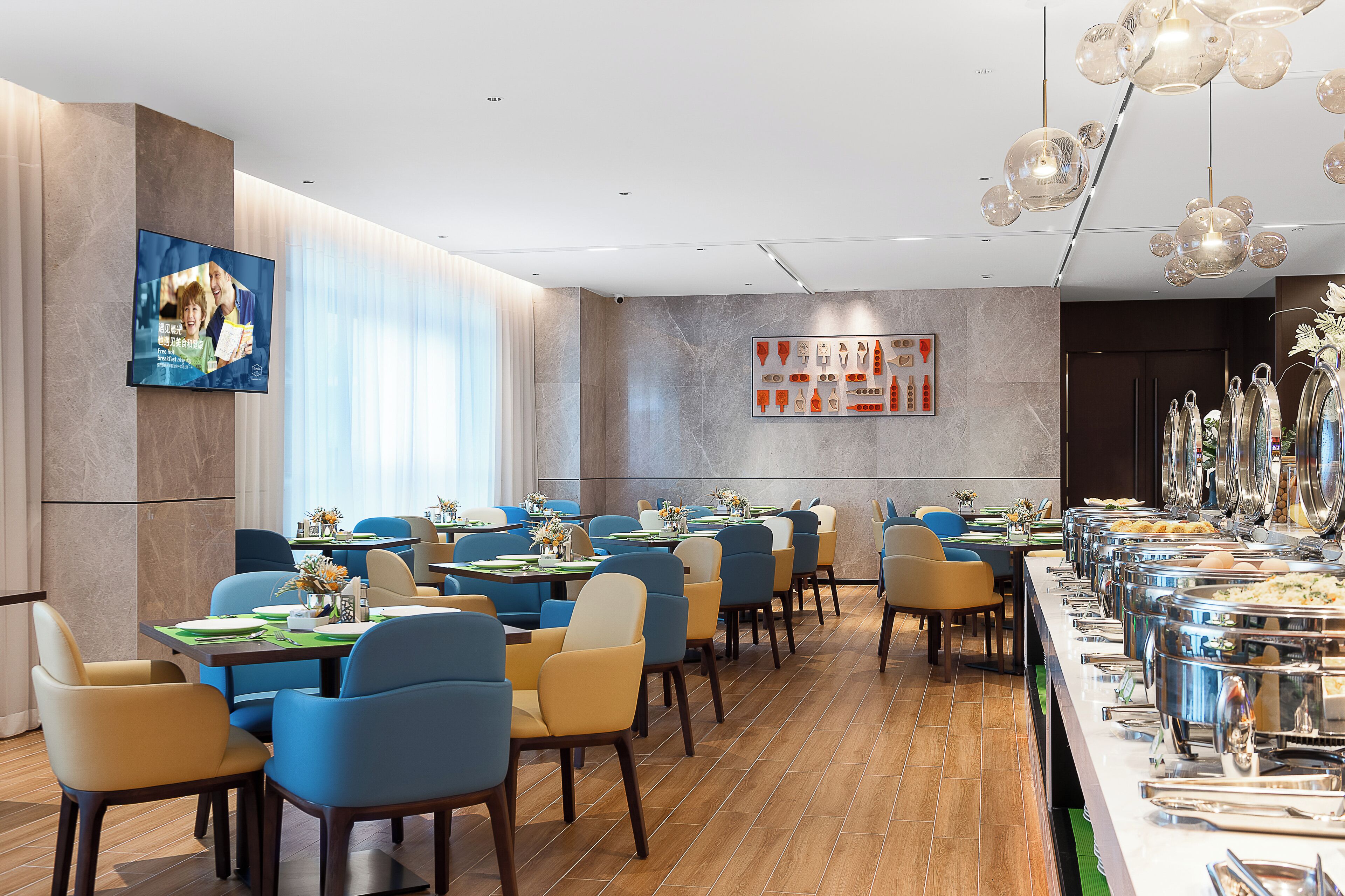 A modern dining area with multiple tables, chairs, and a buffet line with various dishes.